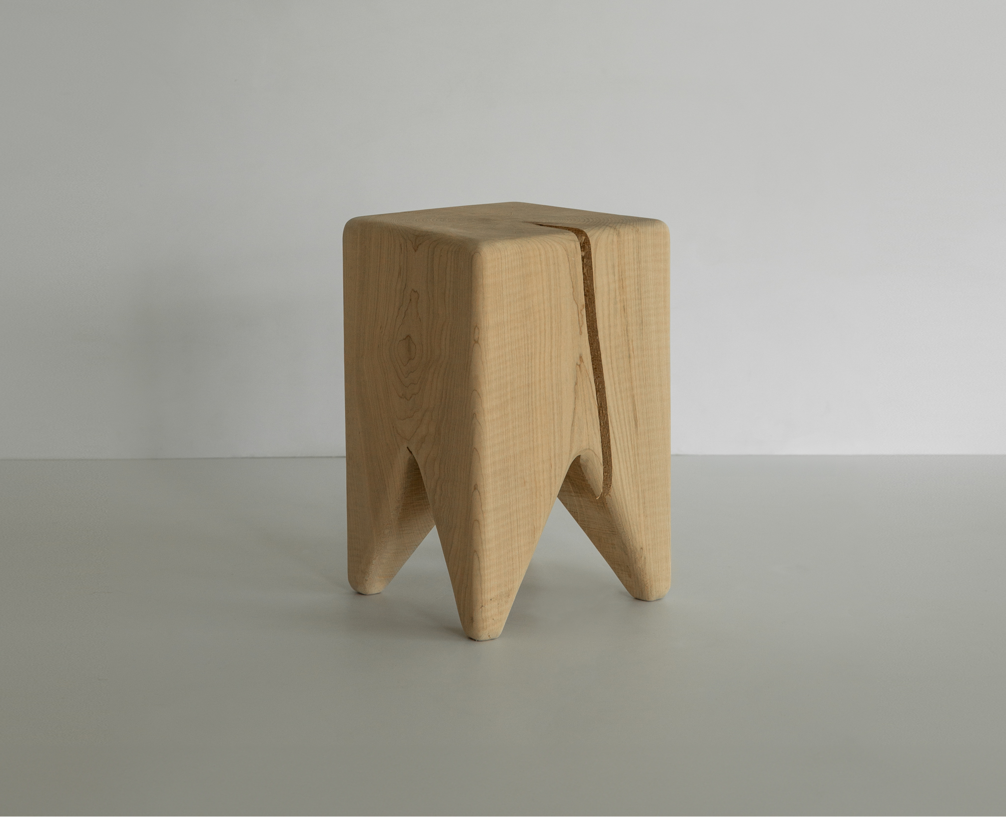A close-up of a wooden block stool with a cross-cut crack and grain on top, natural wood.