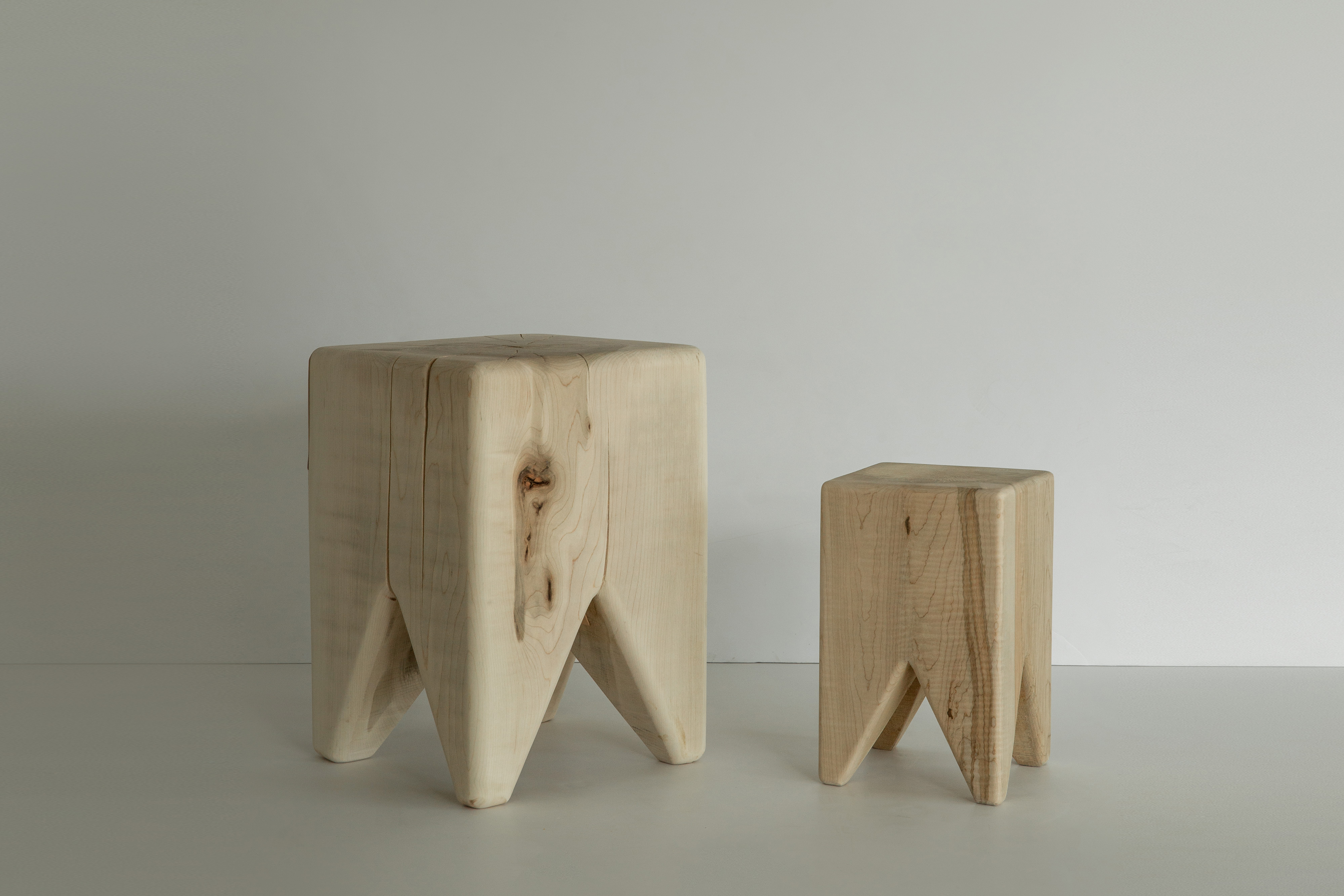 A single large wooden stool with a wide top and triangular legs in a neutral setting.