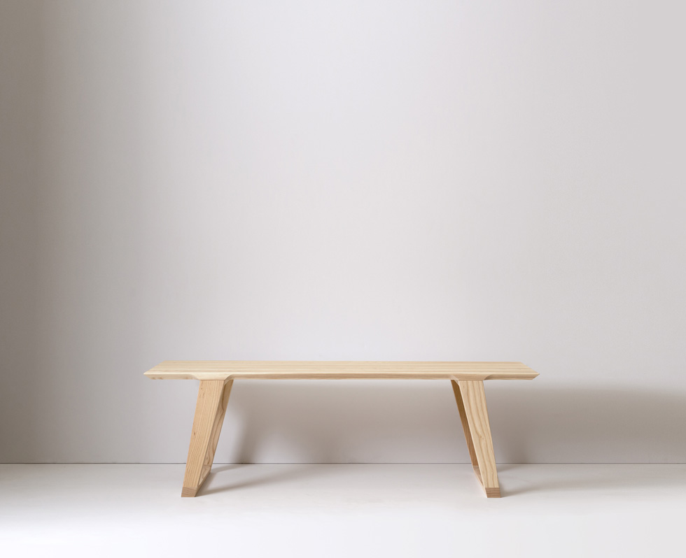 A small wooden bench with angled legs in a bright room