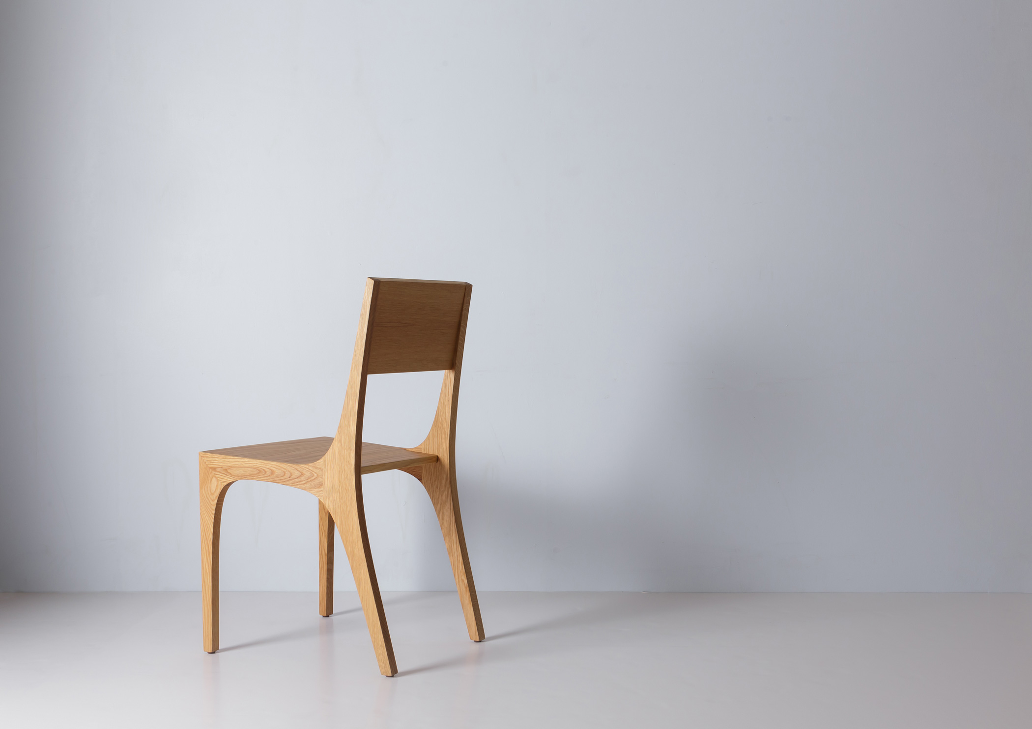 A wooden chair with a simple angular design, showing a solid wood seat, backrest, and four legs in a light oak finish.