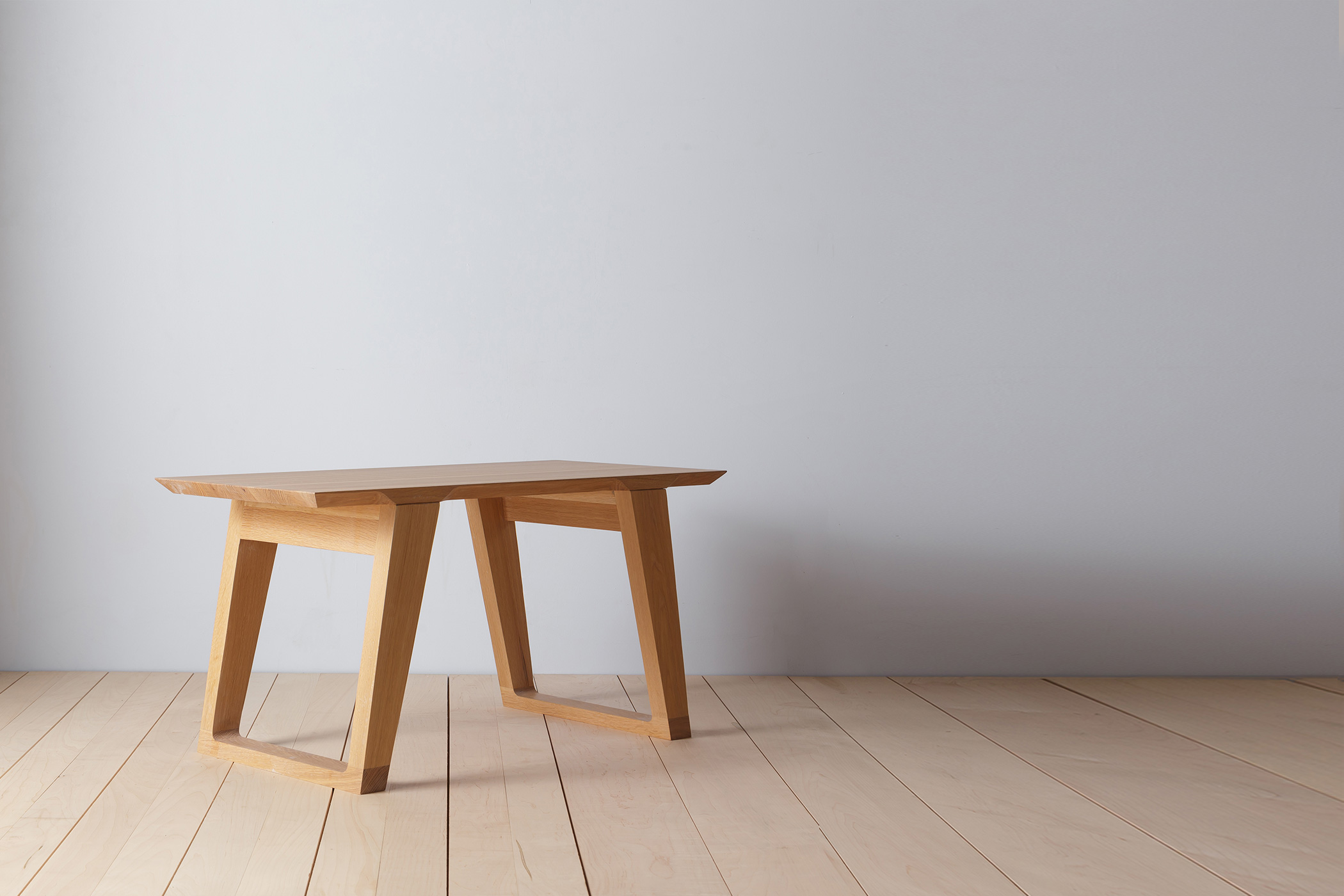 A wooden table with angled legs in a minimal studio setting