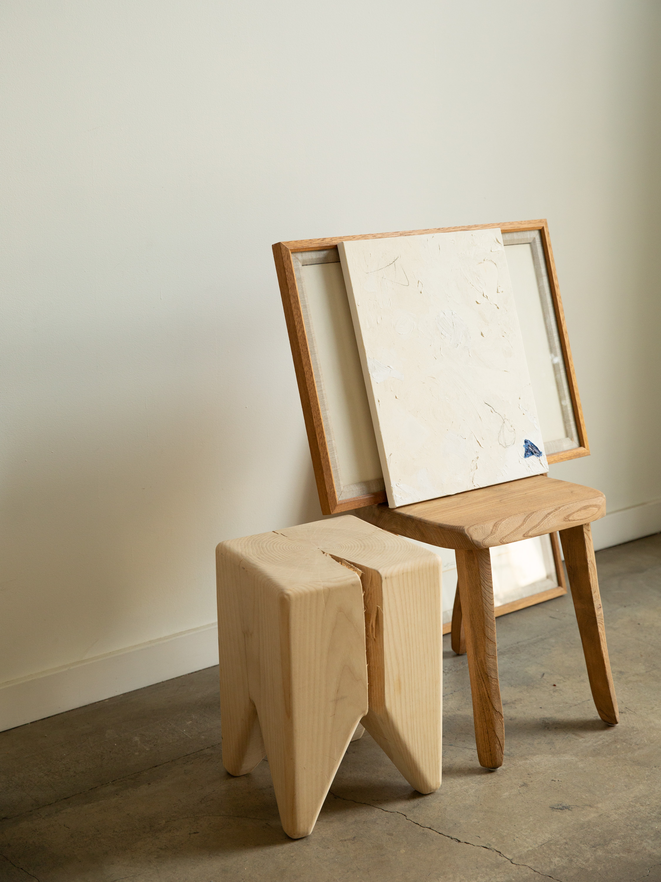 A single wooden stool with unique split in the top, set against a white wall.