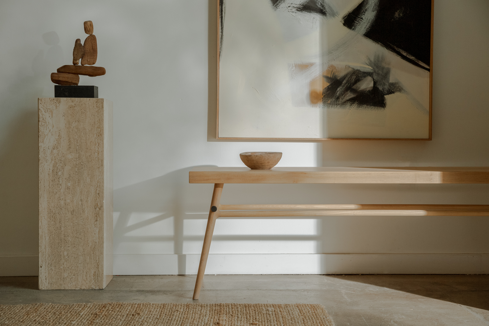 A wooden bench with a flat top on two-tier legs, used as a desk in a bright interior; a ceramic cup and book on the surface.