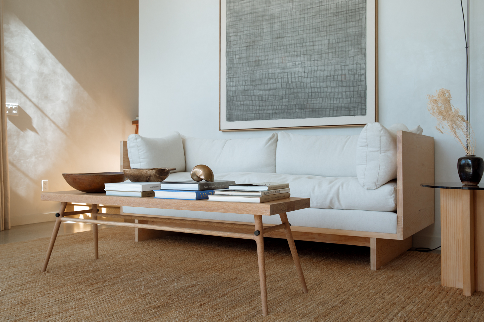 Stack of design books and a wooden bowl on a small wooden table with natural fiber rug.
