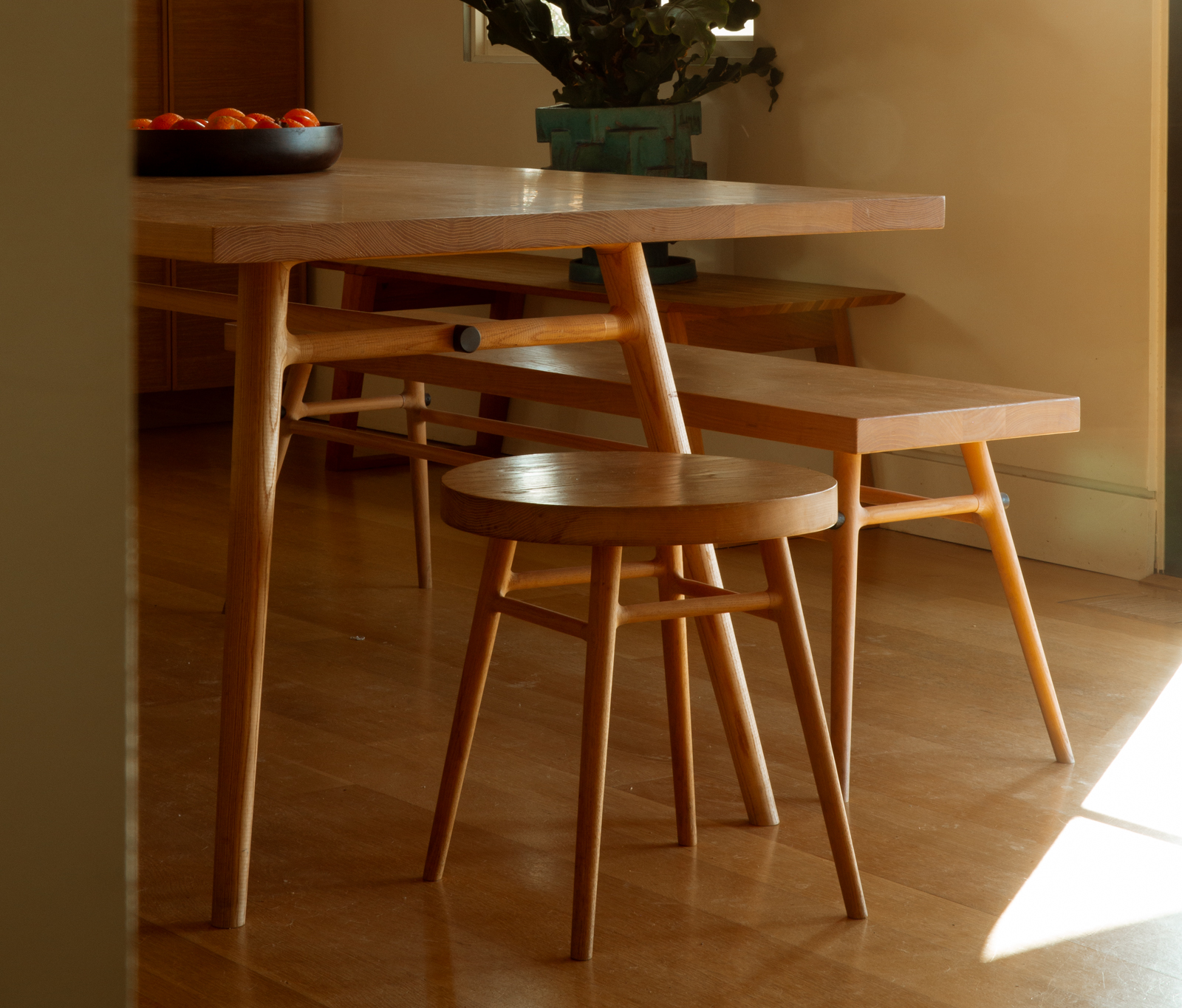 Long wooden dining table in a neutral studio setting with benches underneath.