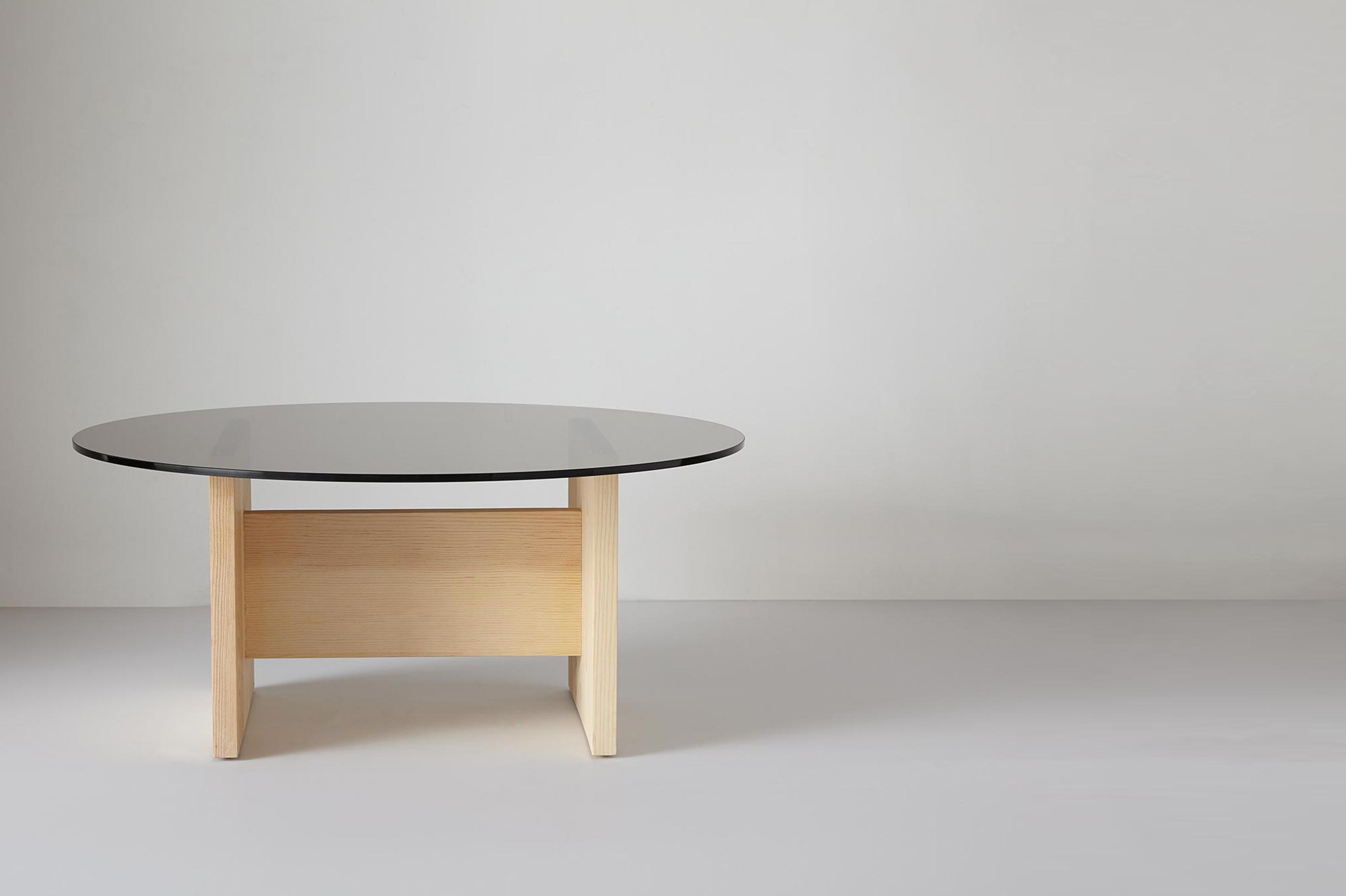 Round glass coffee table with light wood rectangular base, modern minimalist design