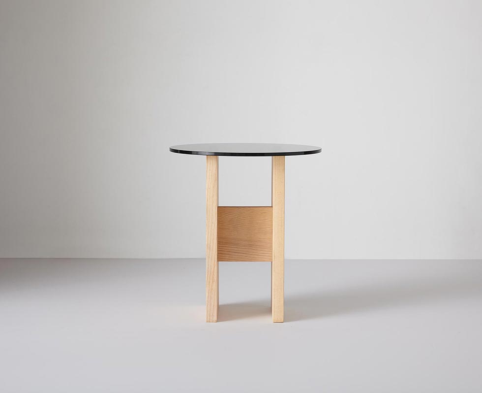 Side table with round glass top on a wooden base, sofa visible