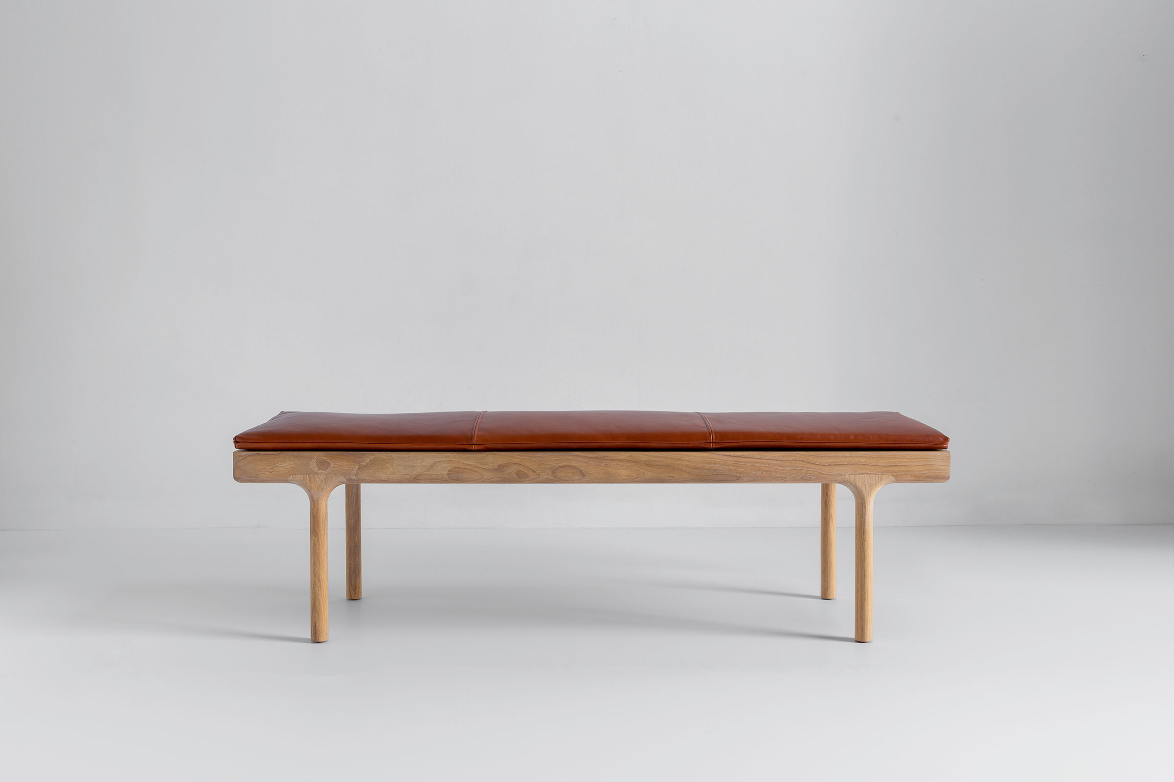 A small wooden bench with brown leather cushion, photographed from a low angle showing a single leg and underside.