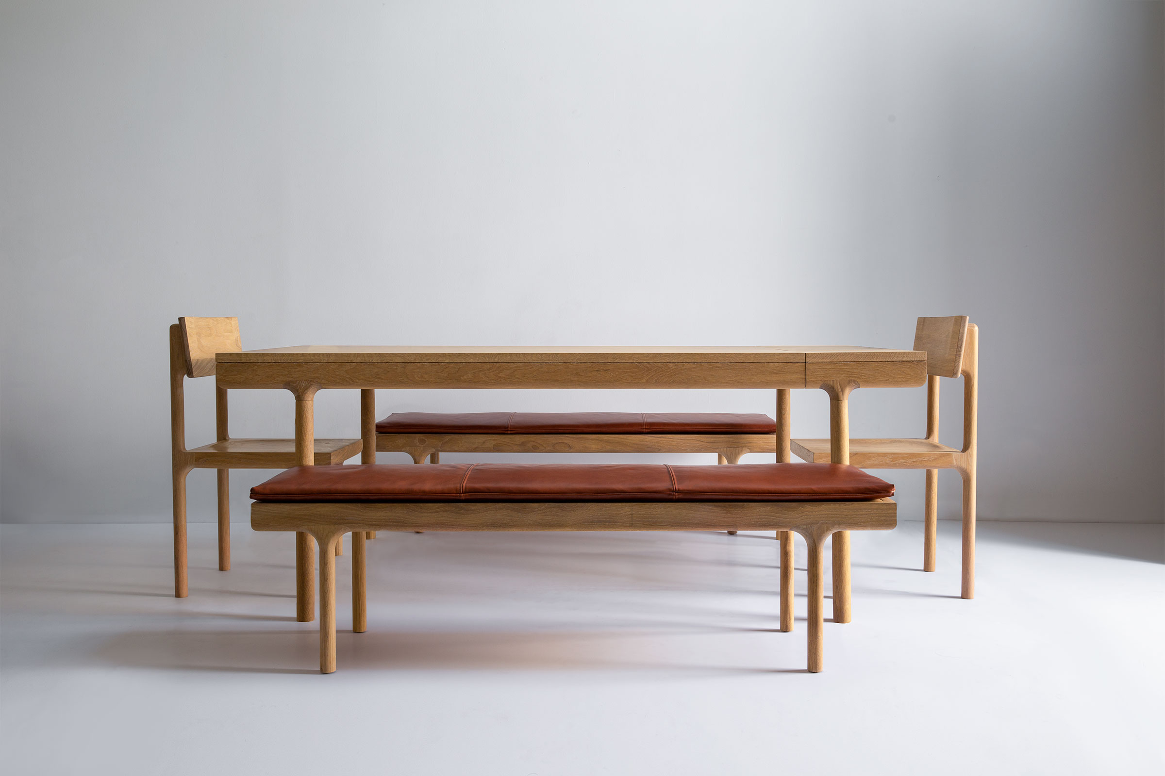 Bench with brown leather cushion and light wood frame photographed against a neutral backdrop.