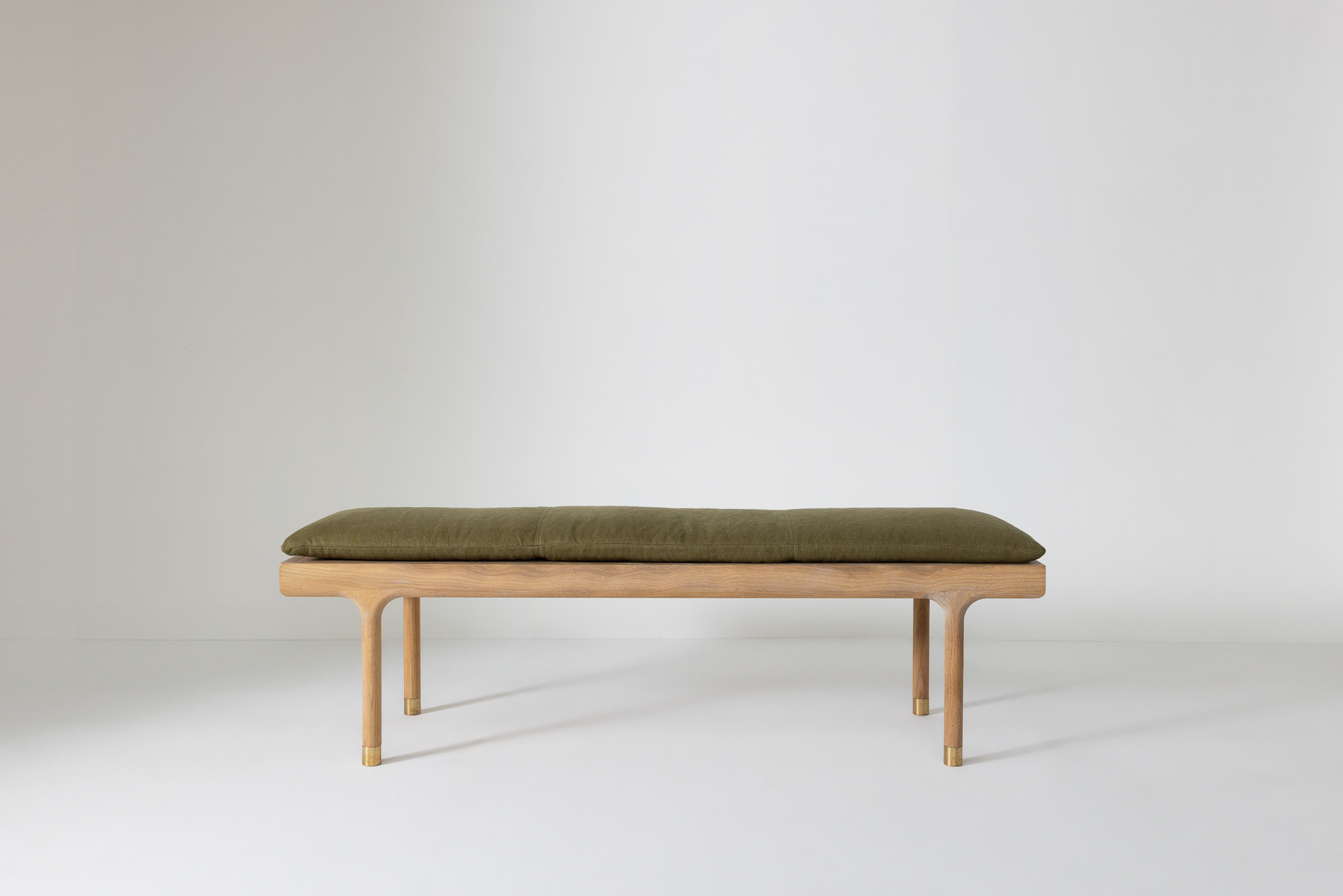 Bench with olive-green leather cushion and light wood frame, set against a clean backdrop.