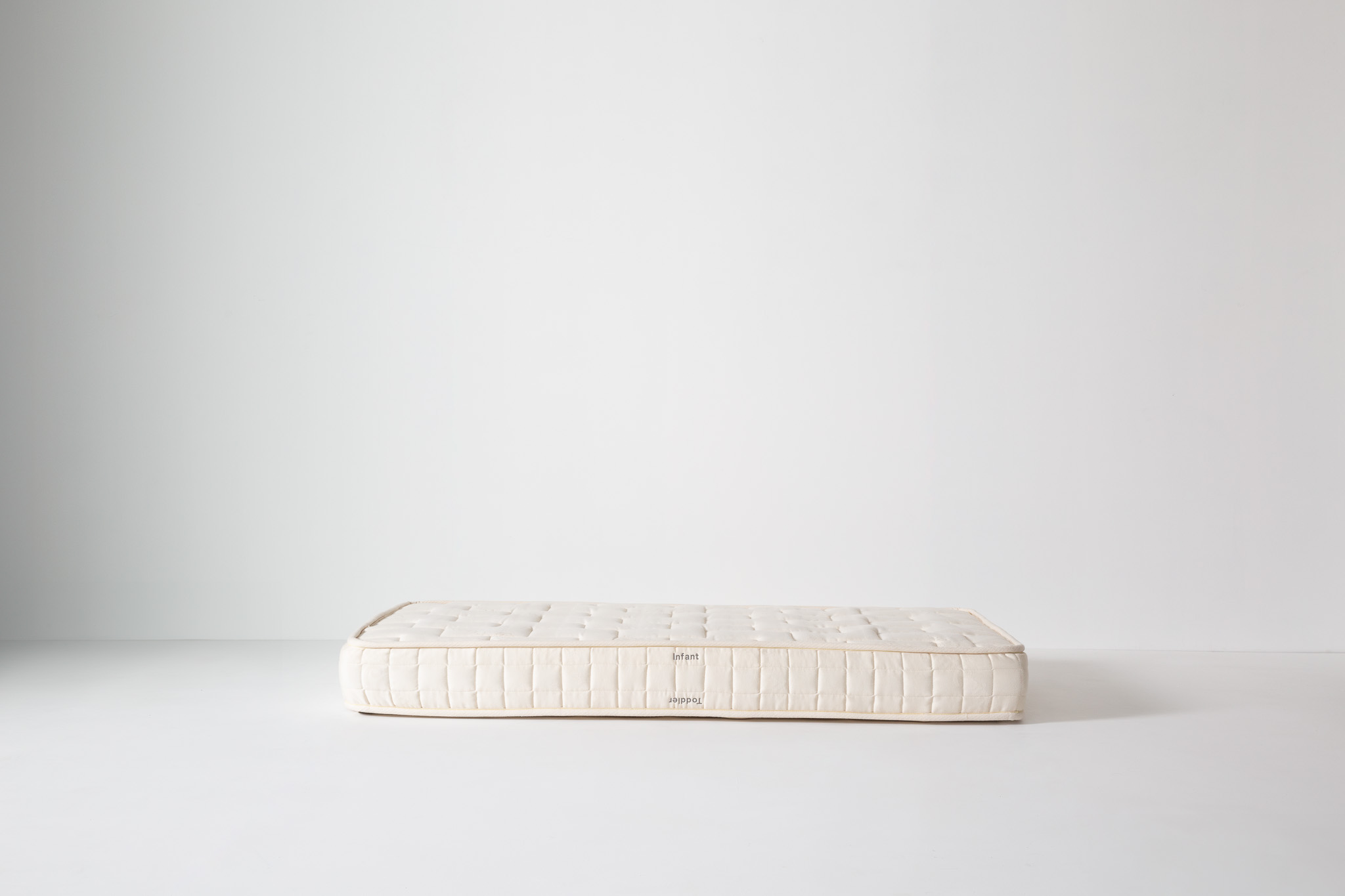 Edge and corner of a white quilted mattress highlighting stitching and side panel.