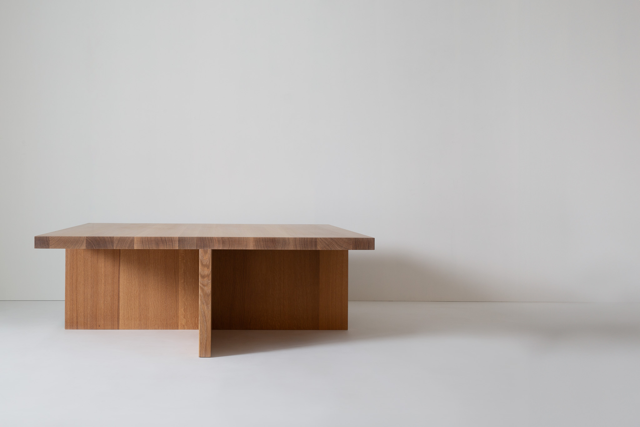A wooden table with a solid rectangular top and thick, block-like legs made of the same wood, showcasing a geometric design.