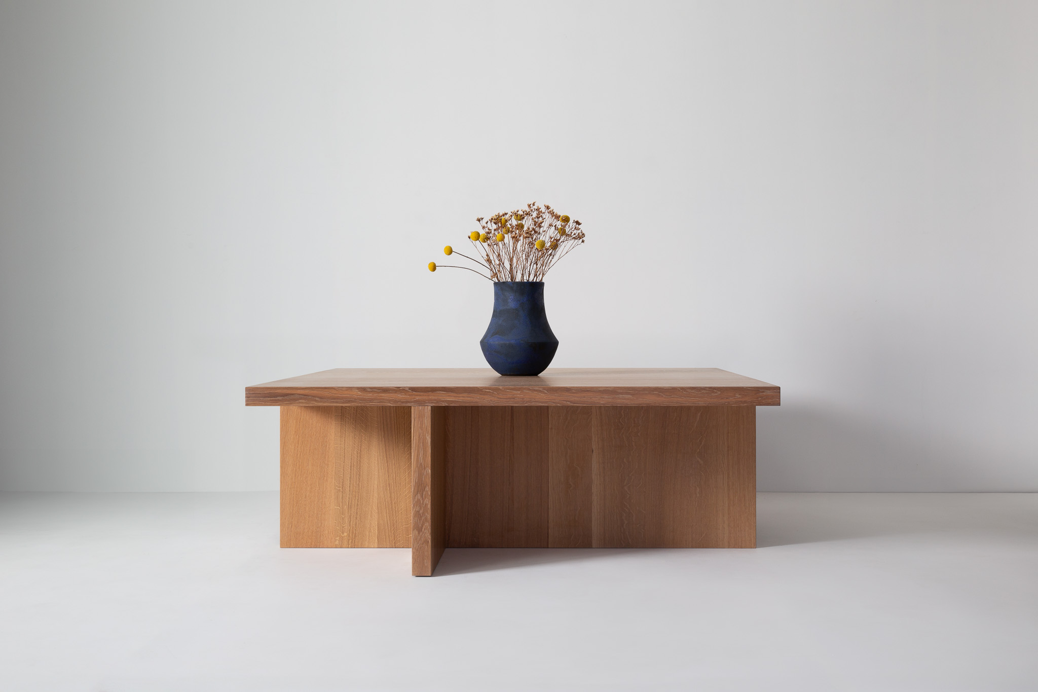 A single small bouquet of yellow flowers in a dark blue vase on a wooden table